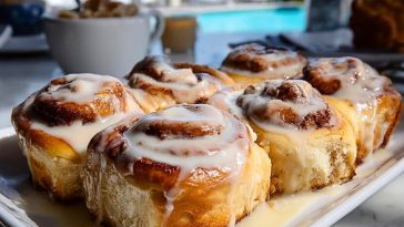 Cinnamon Rolls on a white tray by the pool, dripping with vanilla glaze and showing golden flaky layers.