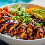 Sliced honey chipotle chicken over white rice with avocado, tomatoes, cucumbers, carrots, and cabbage in a white bowl.