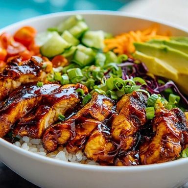 Sliced honey chipotle chicken over white rice with avocado, tomatoes, cucumbers, carrots, and cabbage in a white bowl.