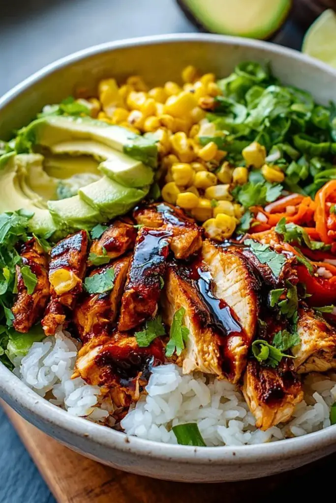 Grilled honey chipotle chicken on rice, topped with avocado, corn, carrots, herbs, and green onions in a rustic ceramic bowl.