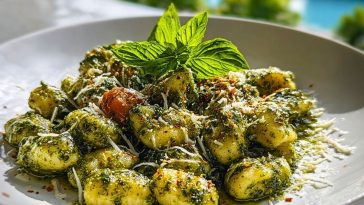 Plate of pesto gnocchi topped with Parmesan, red pepper flakes, cherry tomato, and fresh basil garnish