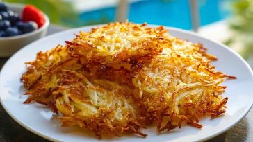 Golden brown Air Fryer Hash Browns stacked on a white plate with berries and a pool in the background.
