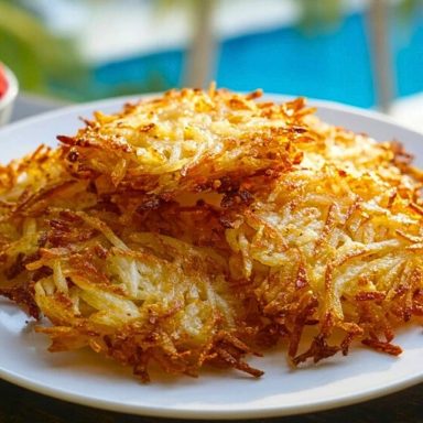 Golden brown Air Fryer Hash Browns stacked on a white plate with berries and a pool in the background.