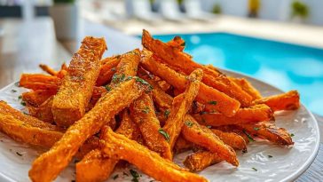 Crispy Air Fryer Sweet Potato Fries stacked on a white plate outdoors by a sunny poolside.