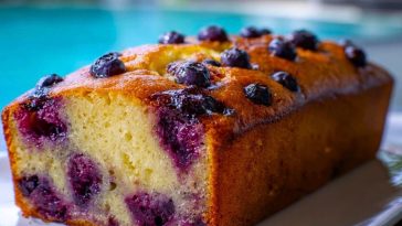Golden blueberry bread loaf by a poolside, bursting with juicy whole blueberries throughout the moist, fluffy crumb.