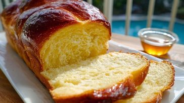 Golden braided Buttery Brioche Bread sliced on a white plate, showing its soft, fluffy texture with a glossy crust.