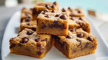Golden chocolate chip cookie bars stacked on a white plate with a soft chewy center and visible chocolate chips, by the seaside.
