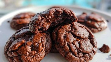 Double Chocolate Cookies stacked on a white plate with melty chocolate chunks and a poolside view