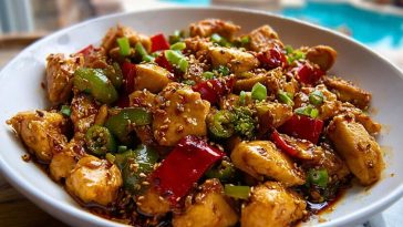 A close-up of Easy Hunan Chicken Recipe with juicy chicken, green and red bell peppers, broccoli, and sesame seeds in a glossy chili garlic sauce.