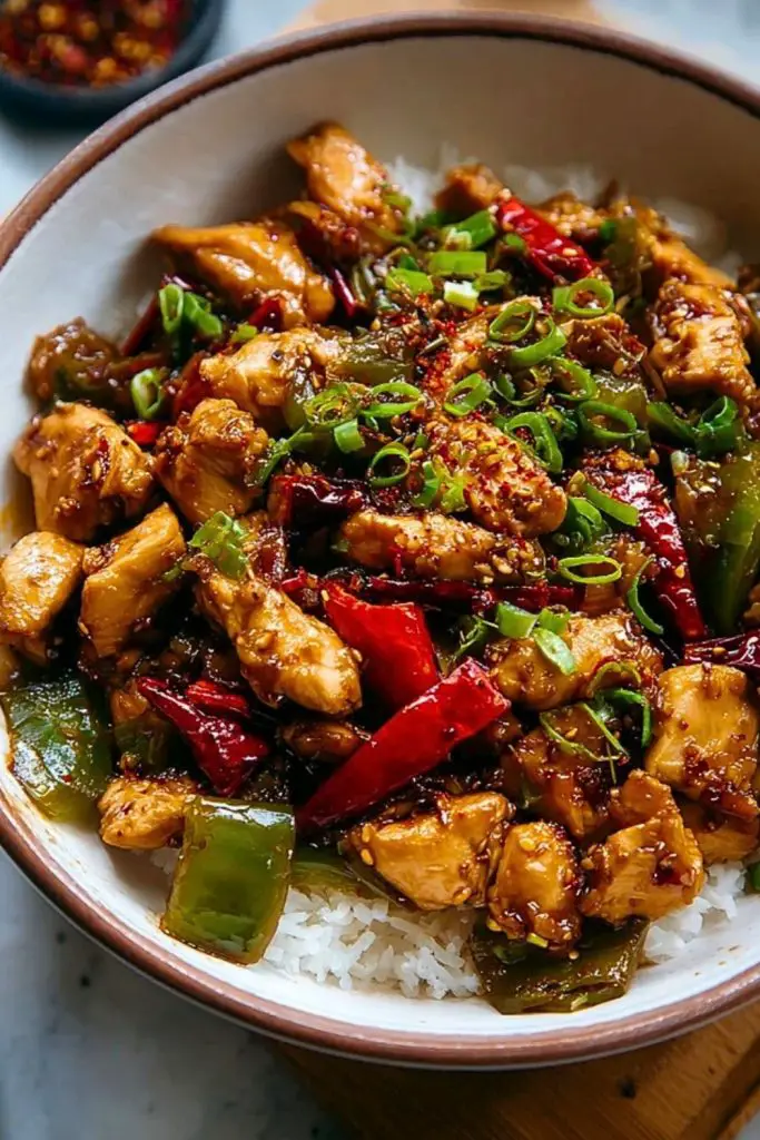 Easy Hunan Chicken Recipe served over white rice in a bowl, topped with scallions, red pepper flakes, and coated in spicy garlic sauce.