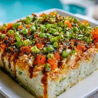 Block-style Easy Sushi Bake served on a white plate, layered with spicy mayo, green onions, tobiko, and drizzled unagi sauce.