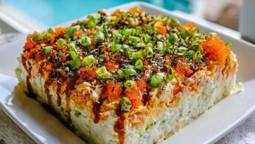 Block-style Easy Sushi Bake served on a white plate, layered with spicy mayo, green onions, tobiko, and drizzled unagi sauce.