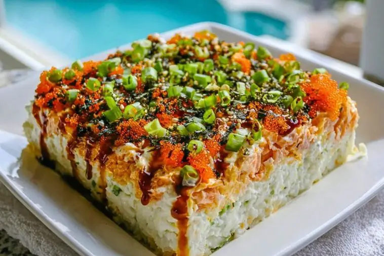 Block-style Easy Sushi Bake served on a white plate, layered with spicy mayo, green onions, tobiko, and drizzled unagi sauce.