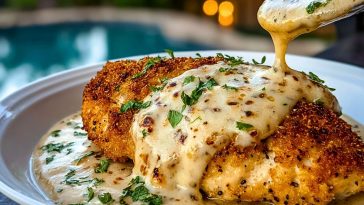 Crispy breaded chicken breasts topped with creamy garlic Parmesan sauce and chopped parsley on a white plate.