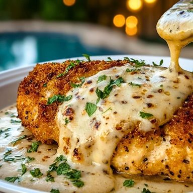 Crispy breaded chicken breasts topped with creamy garlic Parmesan sauce and chopped parsley on a white plate.