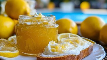 Jar of Italian Lemon Spread Delight on a plate beside a slice of bread topped with lemon spread and cream, with whole lemons in the background.