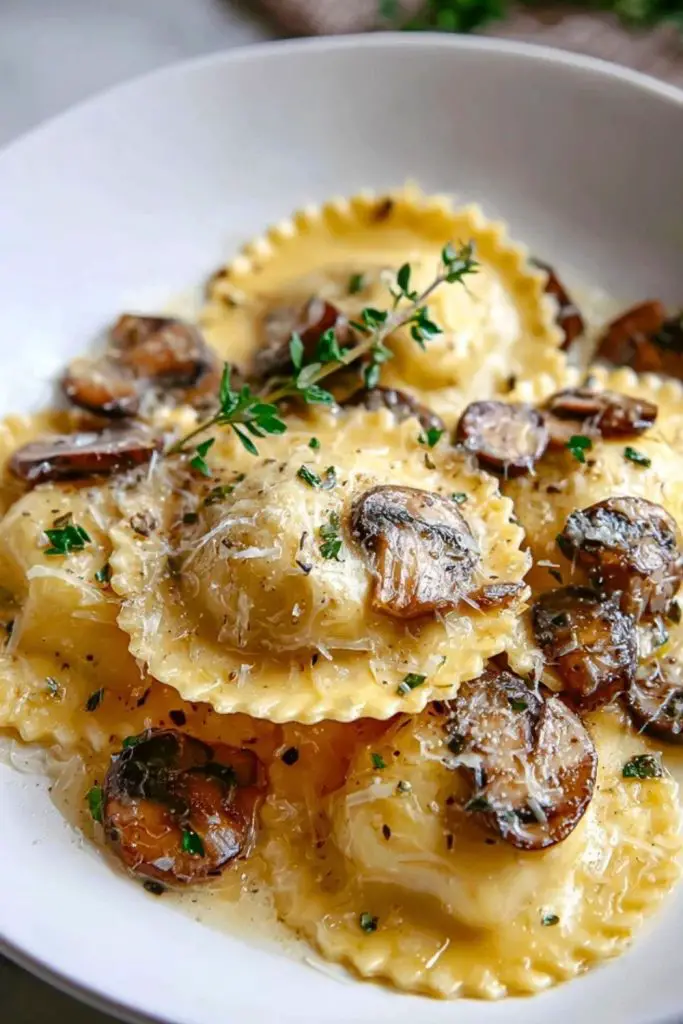 Golden mushroom ravioli coated in garlic Parmesan sauce, garnished with fresh thyme and seared mushrooms in a white bowl.