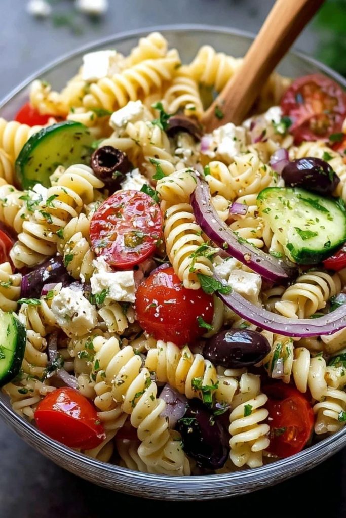Close-up of Pasta Salad with Italian Dressing showing spiral pasta mixed with sliced cucumbers, red onions, cherry tomatoes, and kalamata olives.