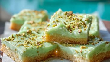Close-up of pistachio pudding sugar cookie bars stacked on a wooden tray, showing the chewy cookie layer and creamy green pistachio topping.