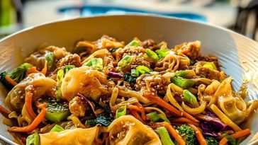 Potsticker Noodle Bowls served in a white bowl with vibrant veggies, sesame seeds, and dumplings under golden sunlight.