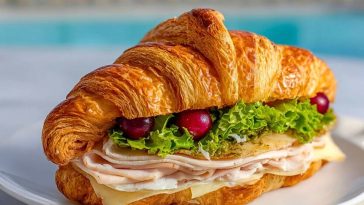 Turkey Croissant Sandwich with cranberries, Swiss cheese, turkey slices, and lettuce on a flaky croissant, served by the pool.