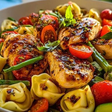 Bowl of Warm Balsamic Chicken Tortellini Salad with grilled chicken breasts, cherry tomatoes, green beans, and tortellini, topped with fresh basil and balsamic glaze.