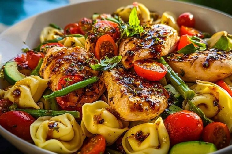 Bowl of Warm Balsamic Chicken Tortellini Salad with grilled chicken breasts, cherry tomatoes, green beans, and tortellini, topped with fresh basil and balsamic glaze.